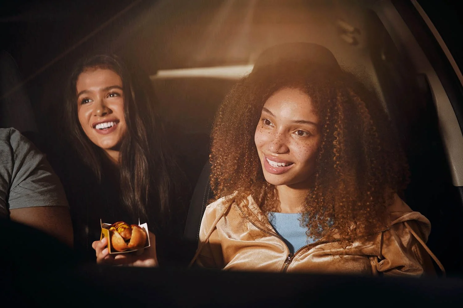 A women enjoys some food whilst on a journey in a car. Taken by advertising photographer Jon Enoch