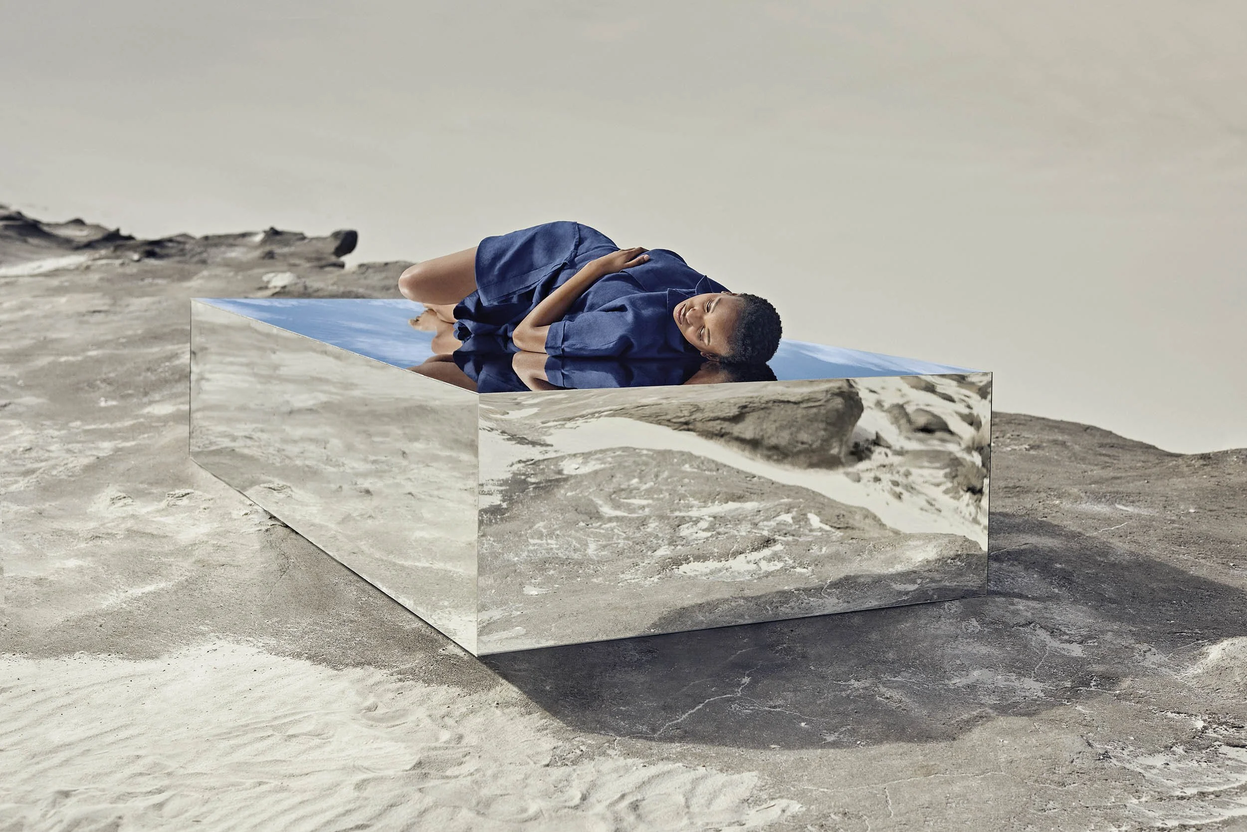 A women sleeps on top of a huge mirrored box in the desert in this advertising image by Jon Enoch