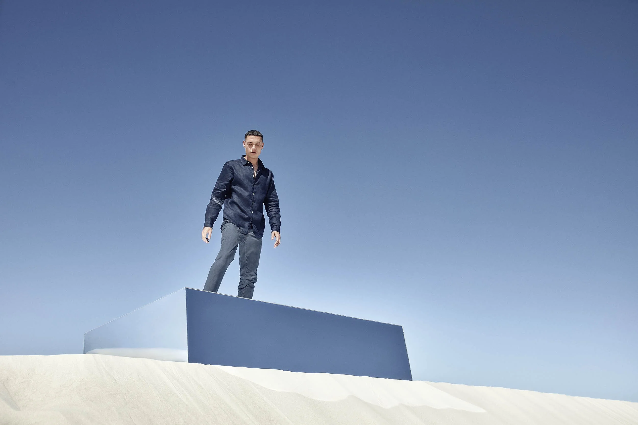 A man stands on top of a mirror and overlooks the big drop in sand dunes in this lifestyle image by Jon Enoch