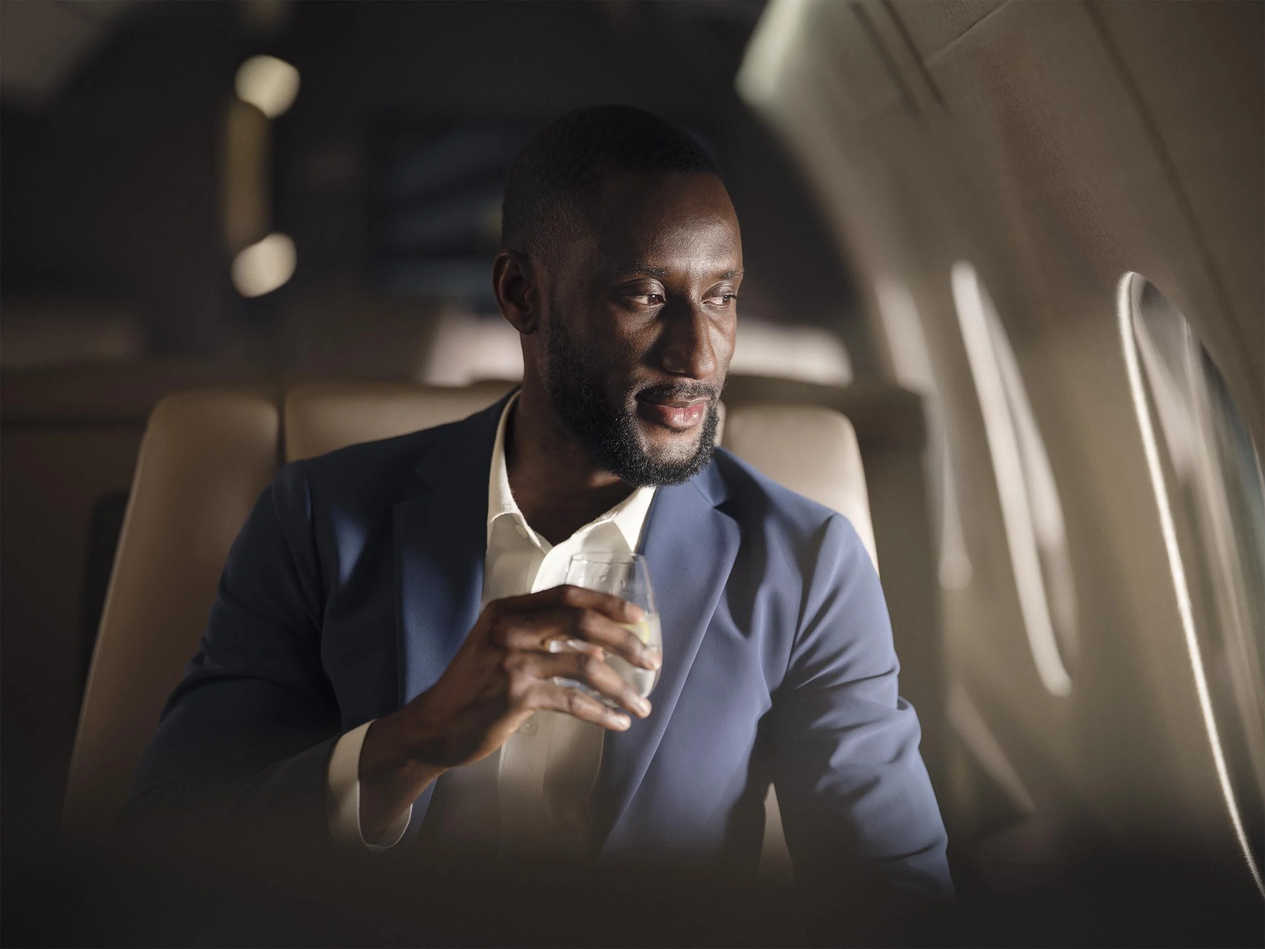 A pasanger enjoys a drink as he looks out of the window onboard a private jet operated by Qatar Airways in this lifestyle image by Jon Enoch