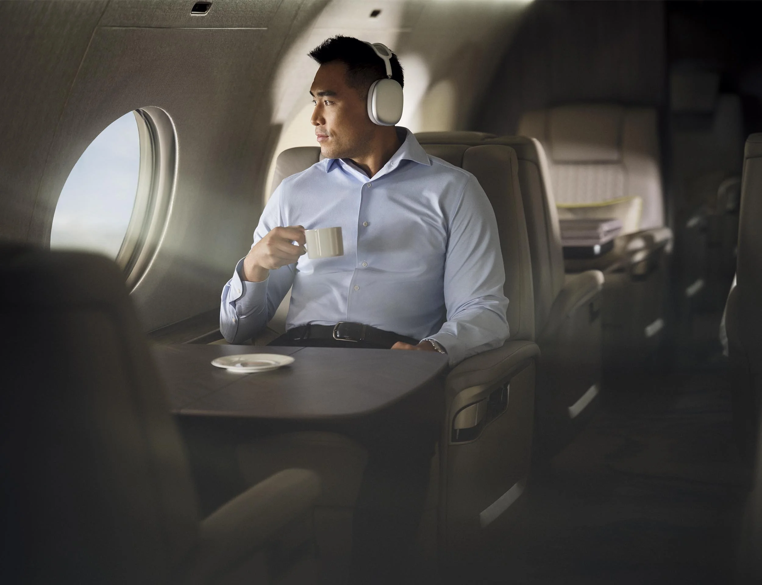 A man sits next to a window with his headphones on enjoying the view out of the large window of a private jet in this lifestyle image by Jon Enoch