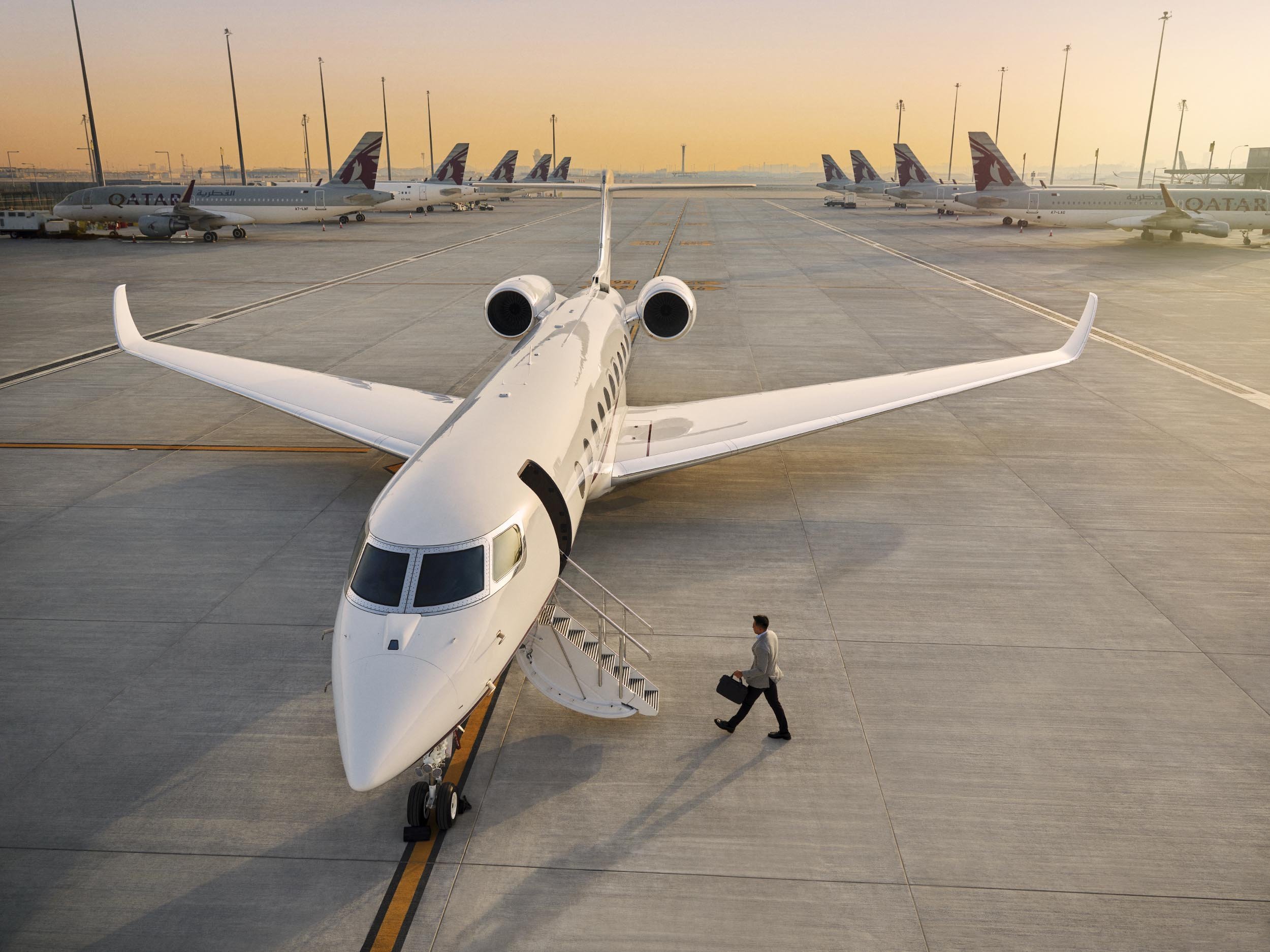 A business passenger is seen walking across the runway towards a private jet as the sun sets in this lifestyle image by Jon Enoch