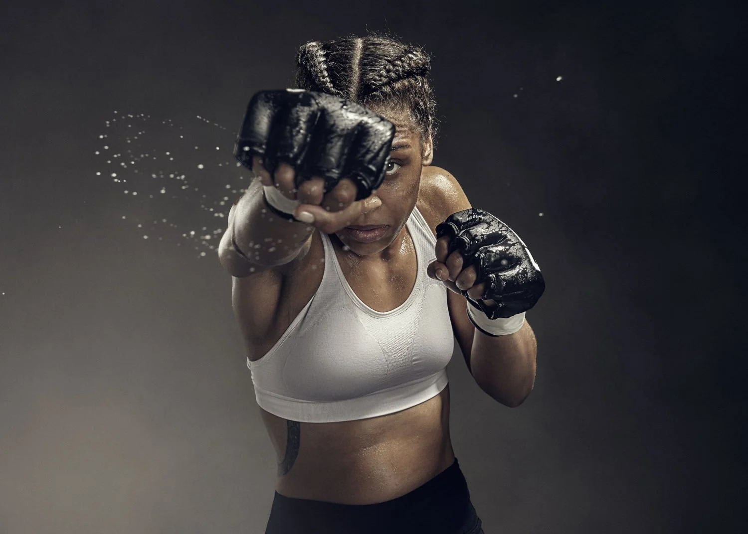 A boxer punches towards the camera, sweat flying from her gloves in this sports photography from Jon Enoch