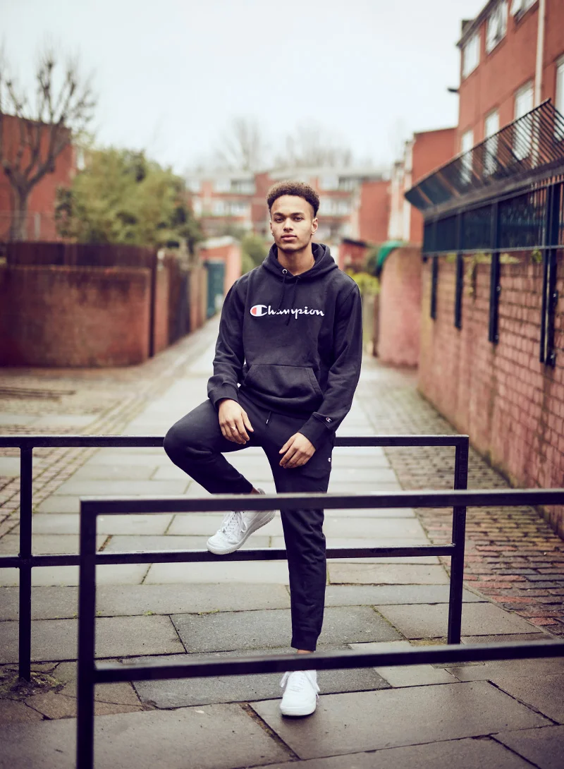 A young man sits on a fence in the urban environment of Peckham, London.