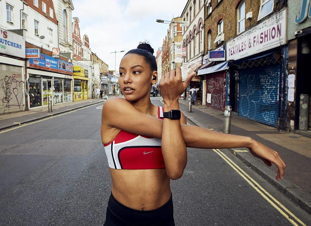 A women stands in peckham high street warming up before a run. Shot by photographer Jon Enoch