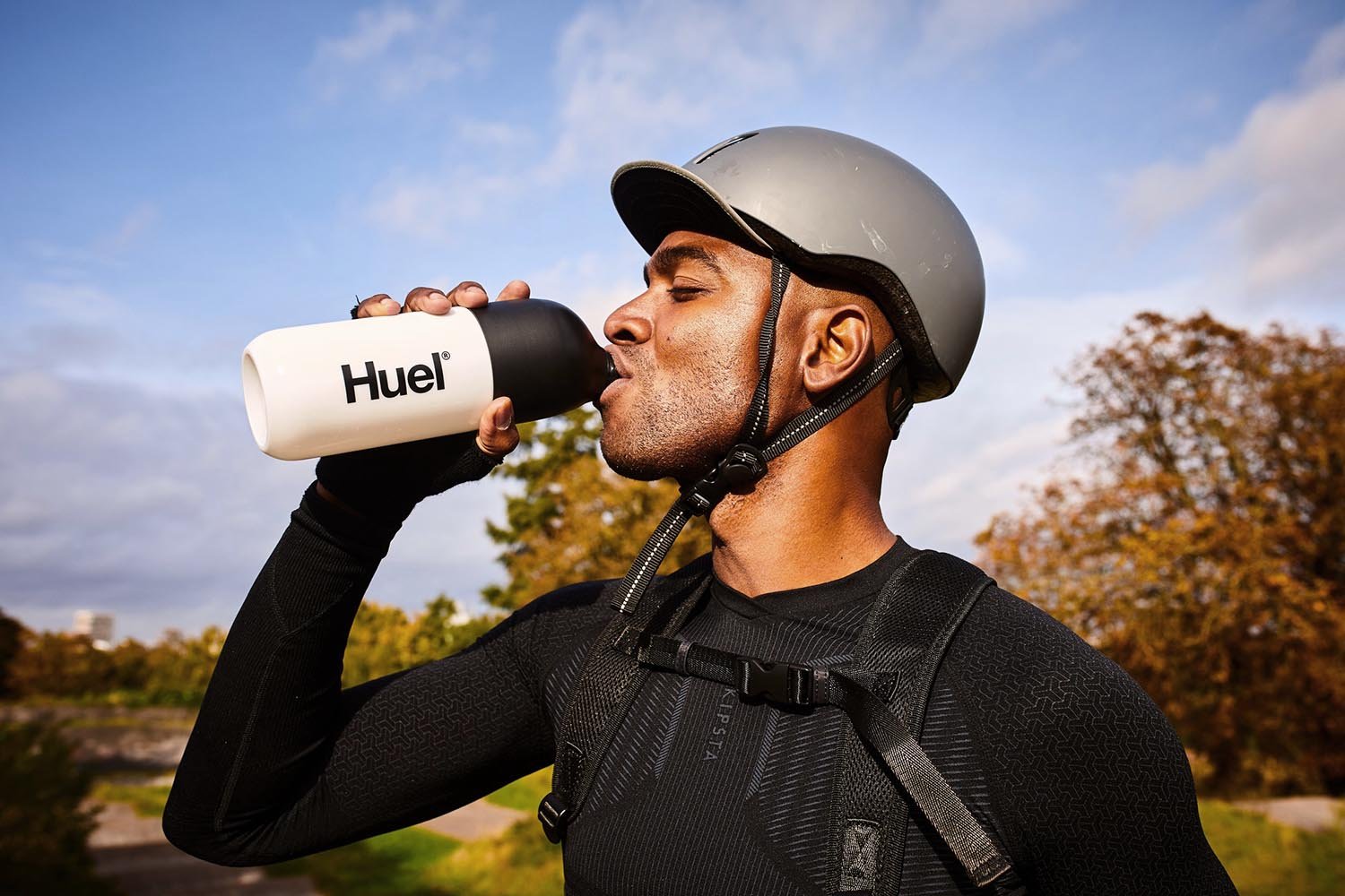 A man drink a bottle of Huel in a park by lifestyle photographer Jon Enoch