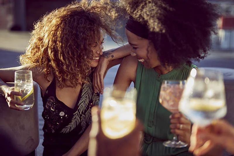 Two friends enjoy a drinks and each others company in the late afternoon sun in the drinks lifestyle image by Jon Enoch