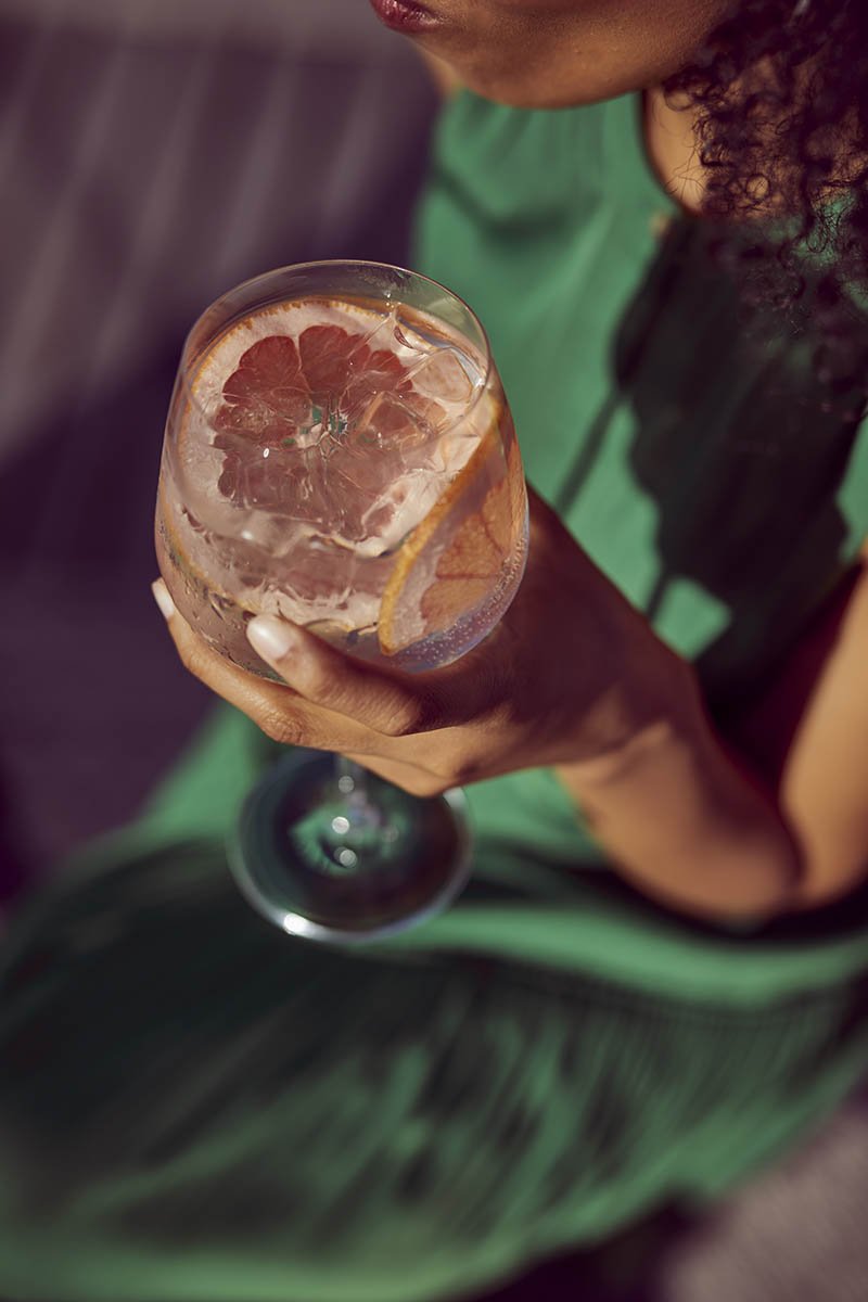 A close up shot of a hand holding a gin and tonic glass in the summer sun in this drinks lifestyle photography by Jon Enoch