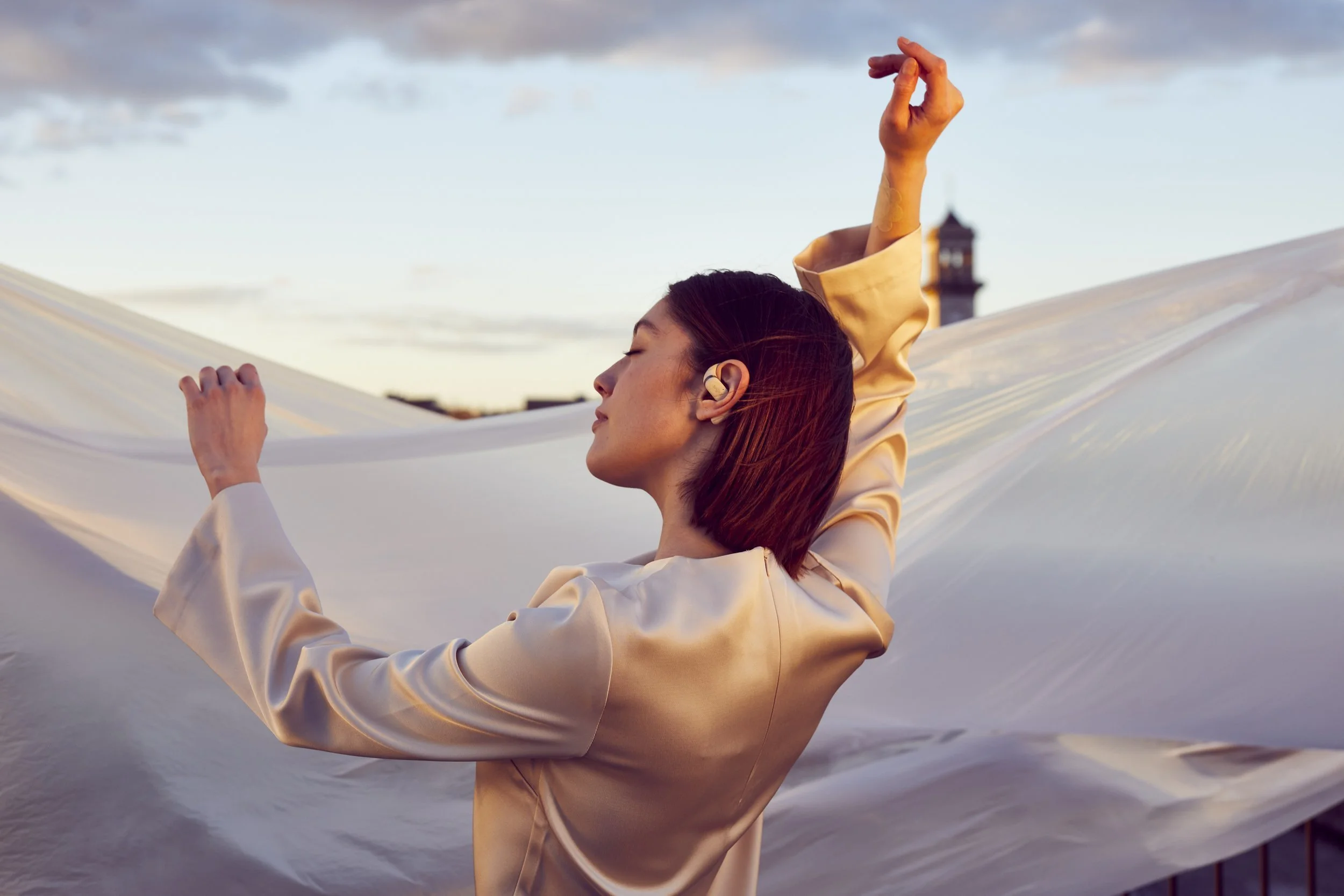 A lifestyle photograph showing a women dances of a roof at sunset whilst listening to music in her headphones