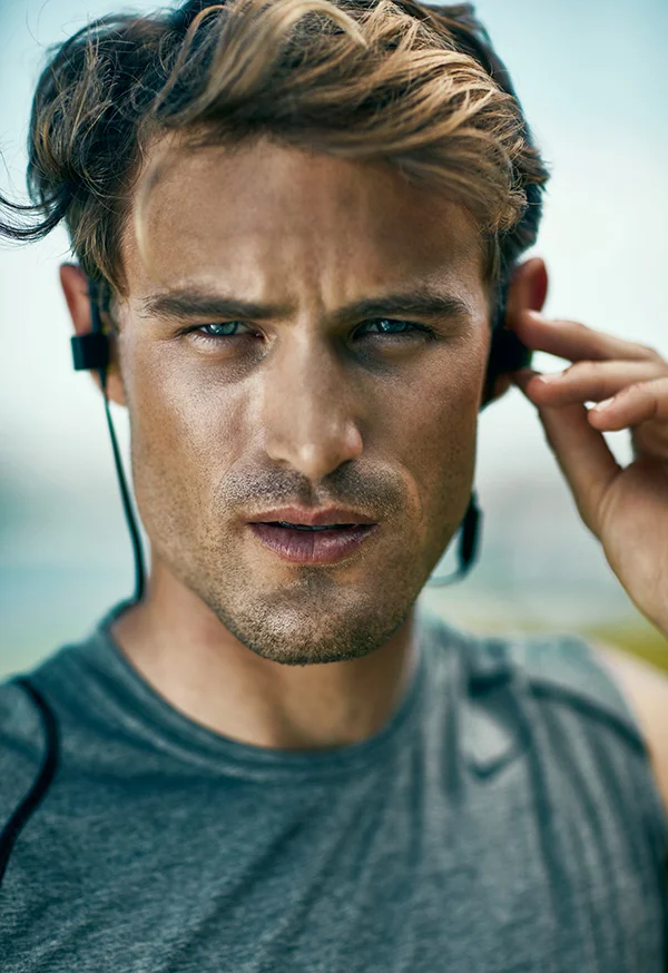 A male athlete put in ear phones to listen to music before starting a run. Jon Enoch sports lifestyle photographer.