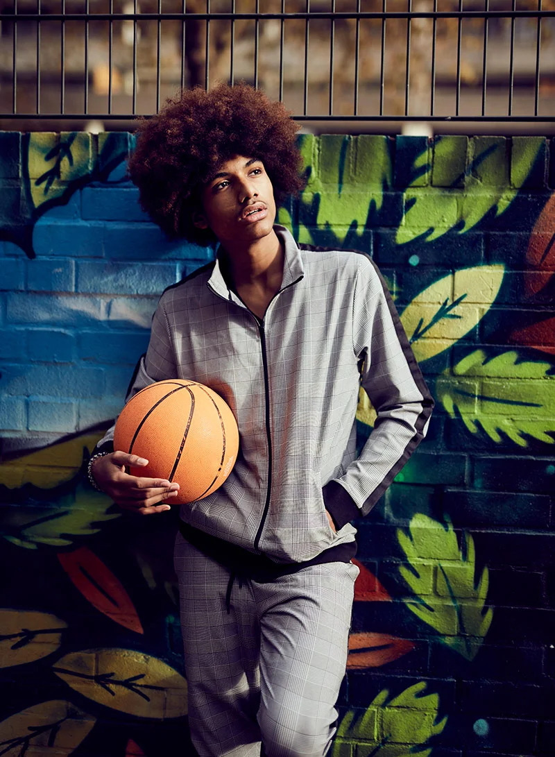 A man with a large afro leans against a colourful wall, holding a basketball under one arm. Image by lifestyle photographer Jon Enoch.