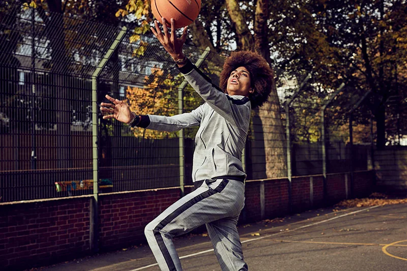 A youth plays basketball on a court in a city setting.
