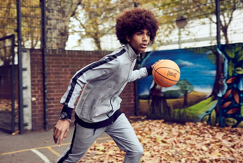 A basket ball player fun across a court surrounded by leaves from a tree. Image taken by London based sport portrait photographer Jon Enoch
