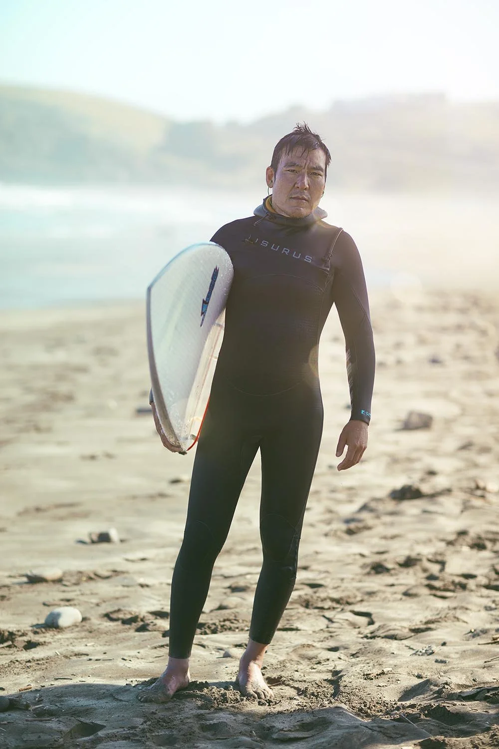 A man poses for a portrait in his wetsuit after going surfing on Pacifica beach. Lifestyle Photographer Jon Enoch.