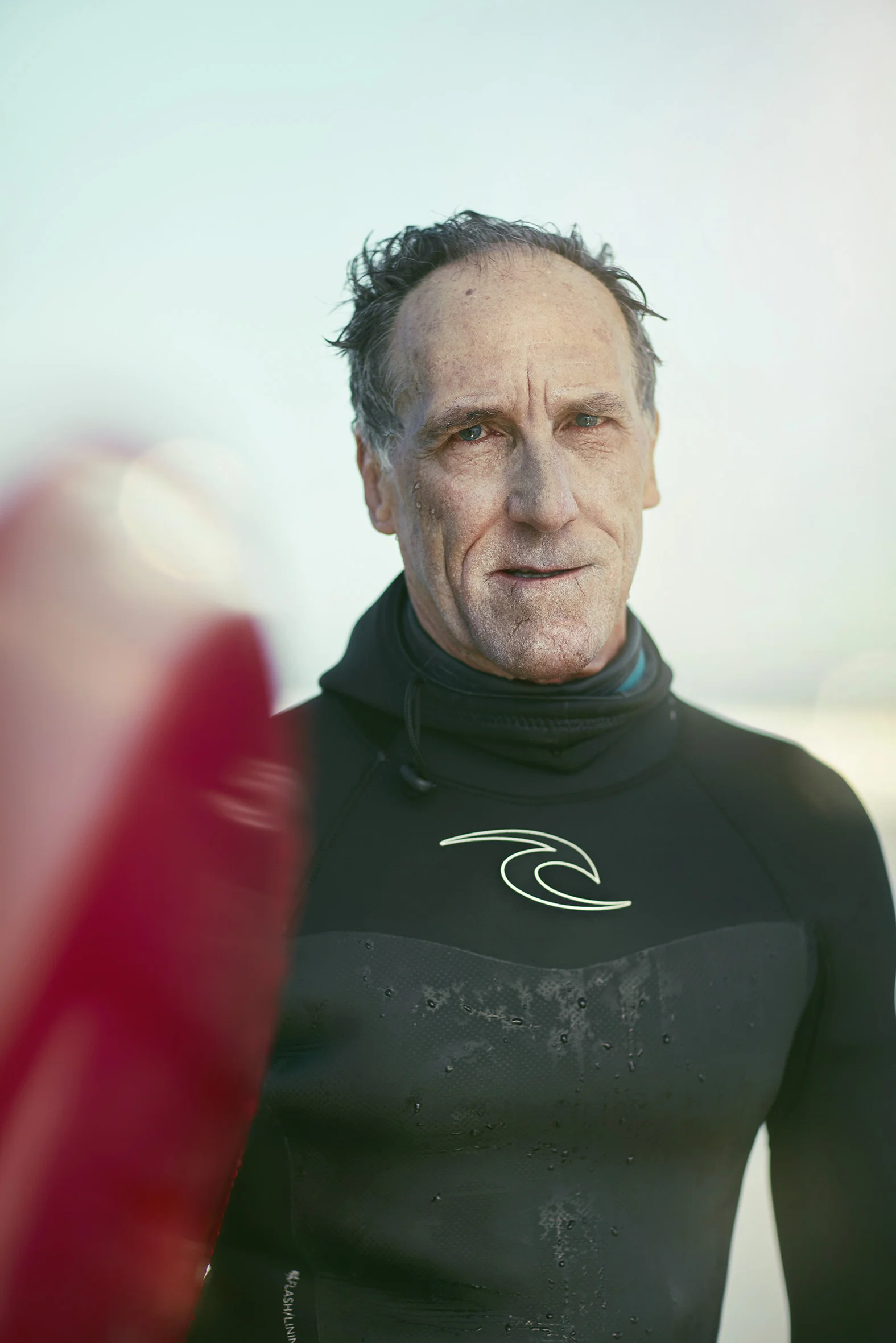 A man poses for a portrait in his wetsuit after going surfing on Pacifica beach. Lifestyle Photographer Jon Enoch.