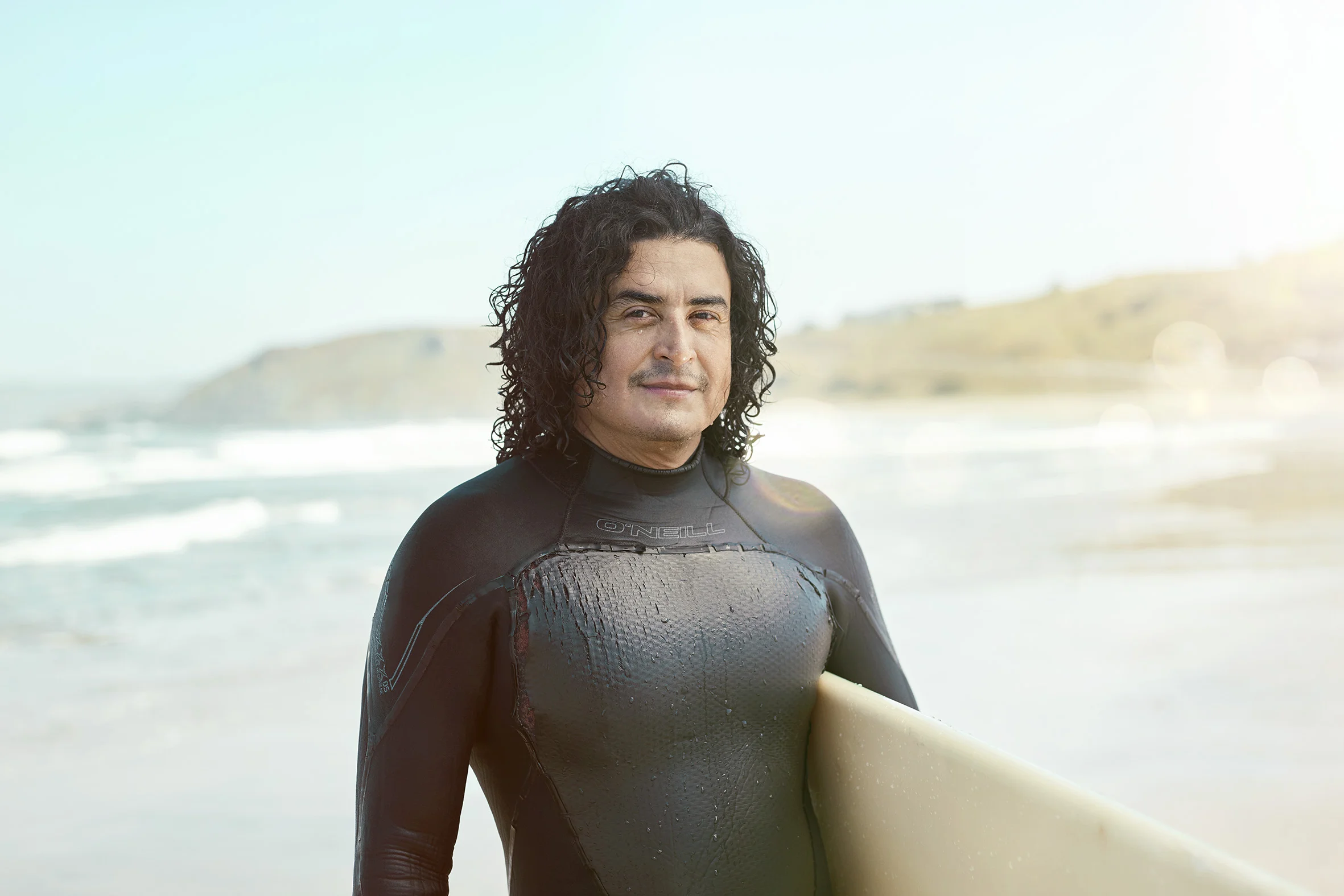 A man poses for a portait in his wetsuit after going surfing on Pacifica beach. Lifestyle Photographer Jon Enoch.
