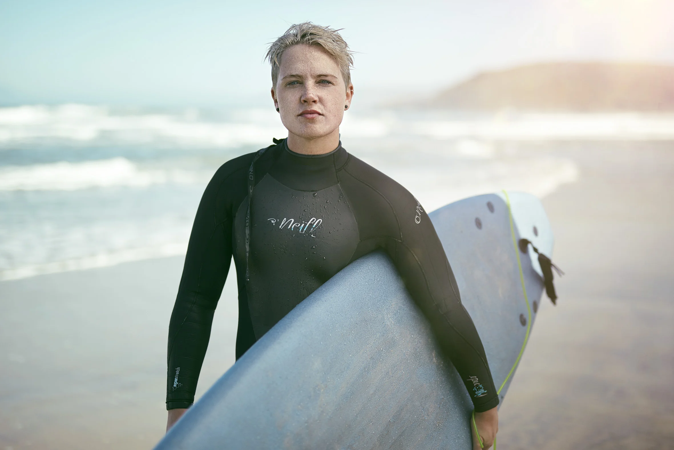 A women poses for a portrait in his wetsuit after going surfing on Pacifica beach. Lifestyle Photographer Jon Enoch.
