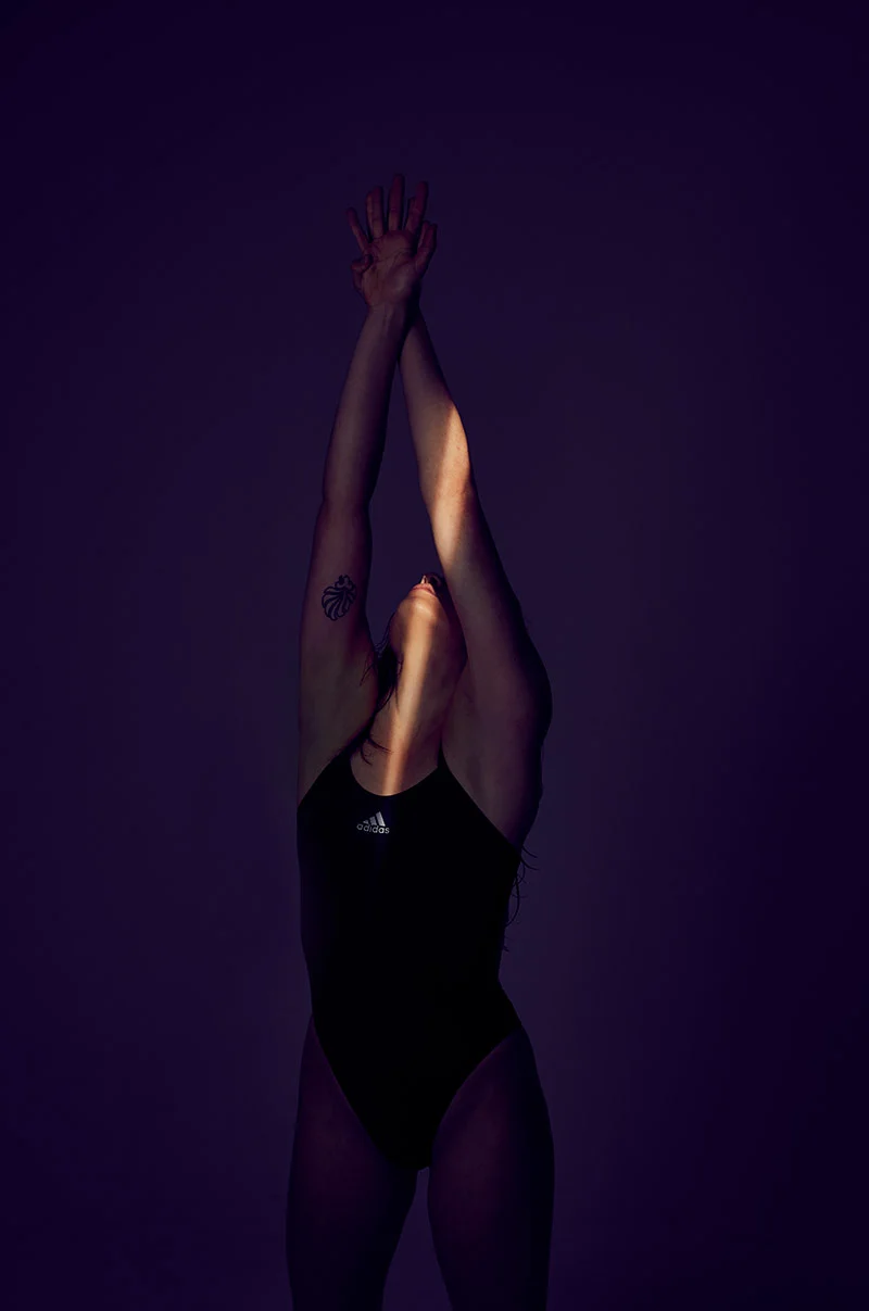A swimmer with a Great Britain tattoo is photographed stretching in a shaft of light. Image taken by advertising photographer Jon Enoch