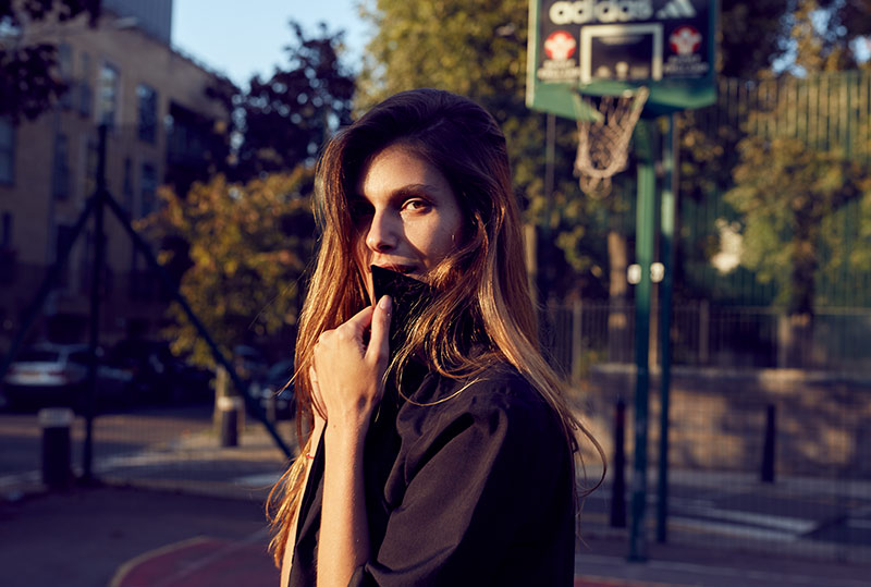 A women pops he collar on a basketball court as the sun sets. Lifestyle photography by Jon Enoch