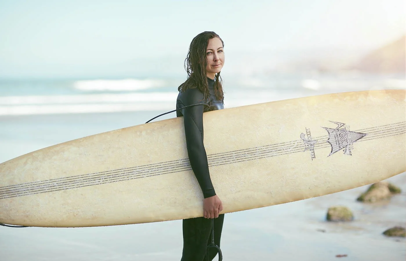 Sport lifestyle photographer Jon Enoch photographs a young women with her long board on the beach in California as the morning sun rises over the beach.