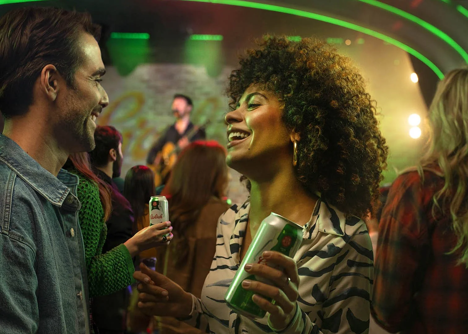 People enjoying a lively concert or party, talking and holding drinks, with a live band playing in the background, colorful neon lights, and a vibrant atmosphere.