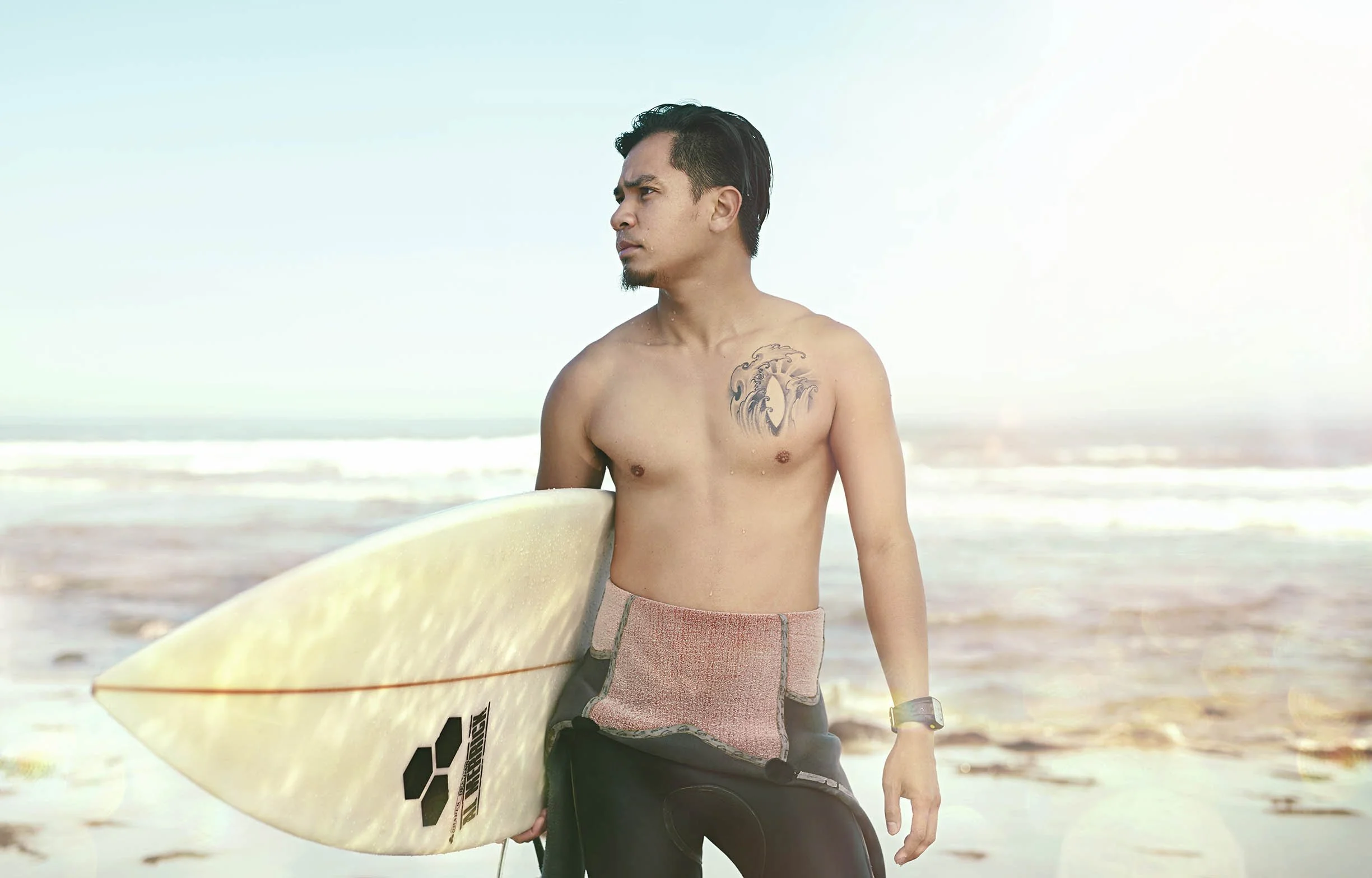 A surfer stands on a beach in California as the sun's rays bounce around him in this lifestyle image shot by Jon Enoch  (Copy)