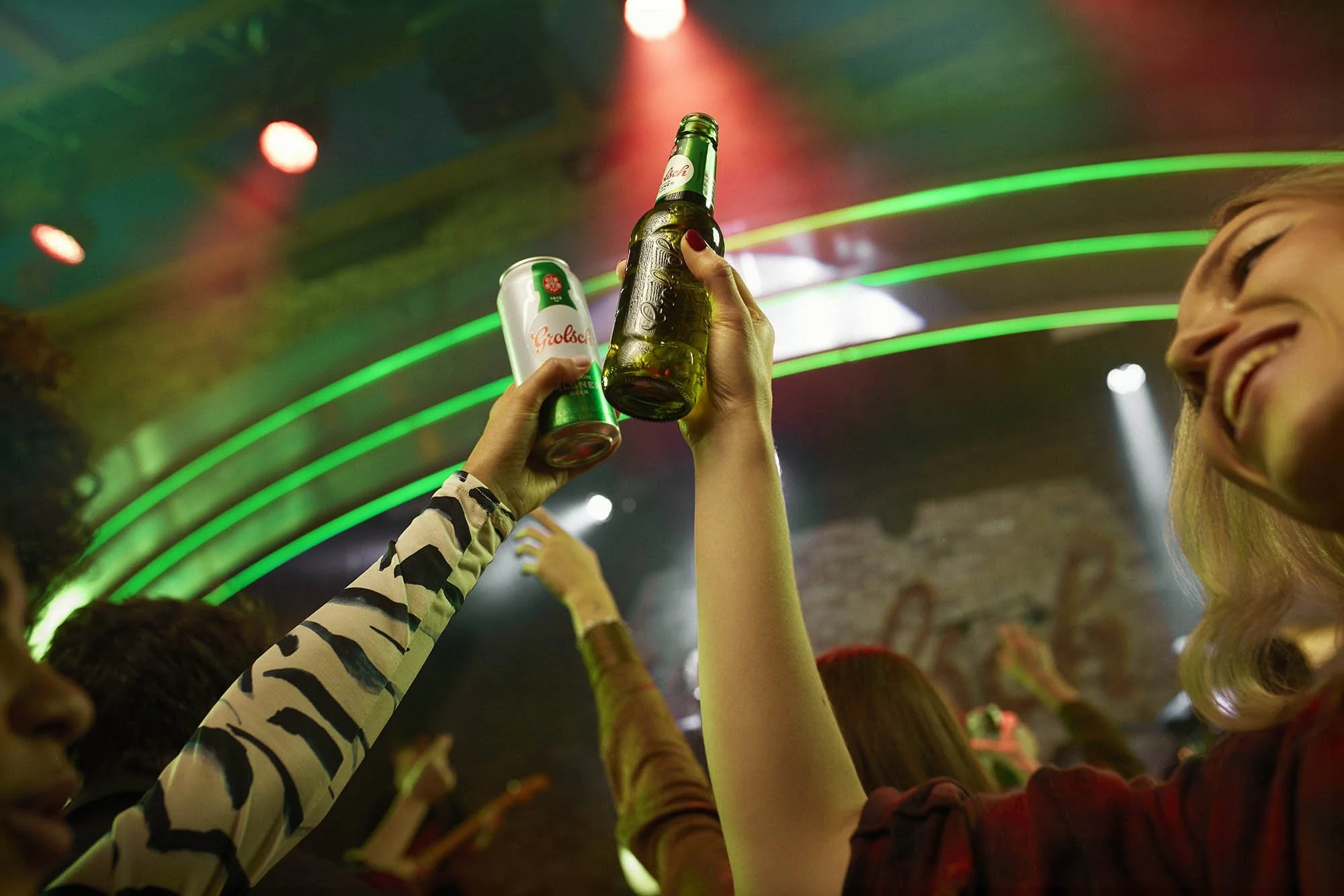 Bottles of beer are raised in the air as a group of friends drink beer whilst watching a band in this fun lifestyle image by London based lifestyle photographer Jon Enoch