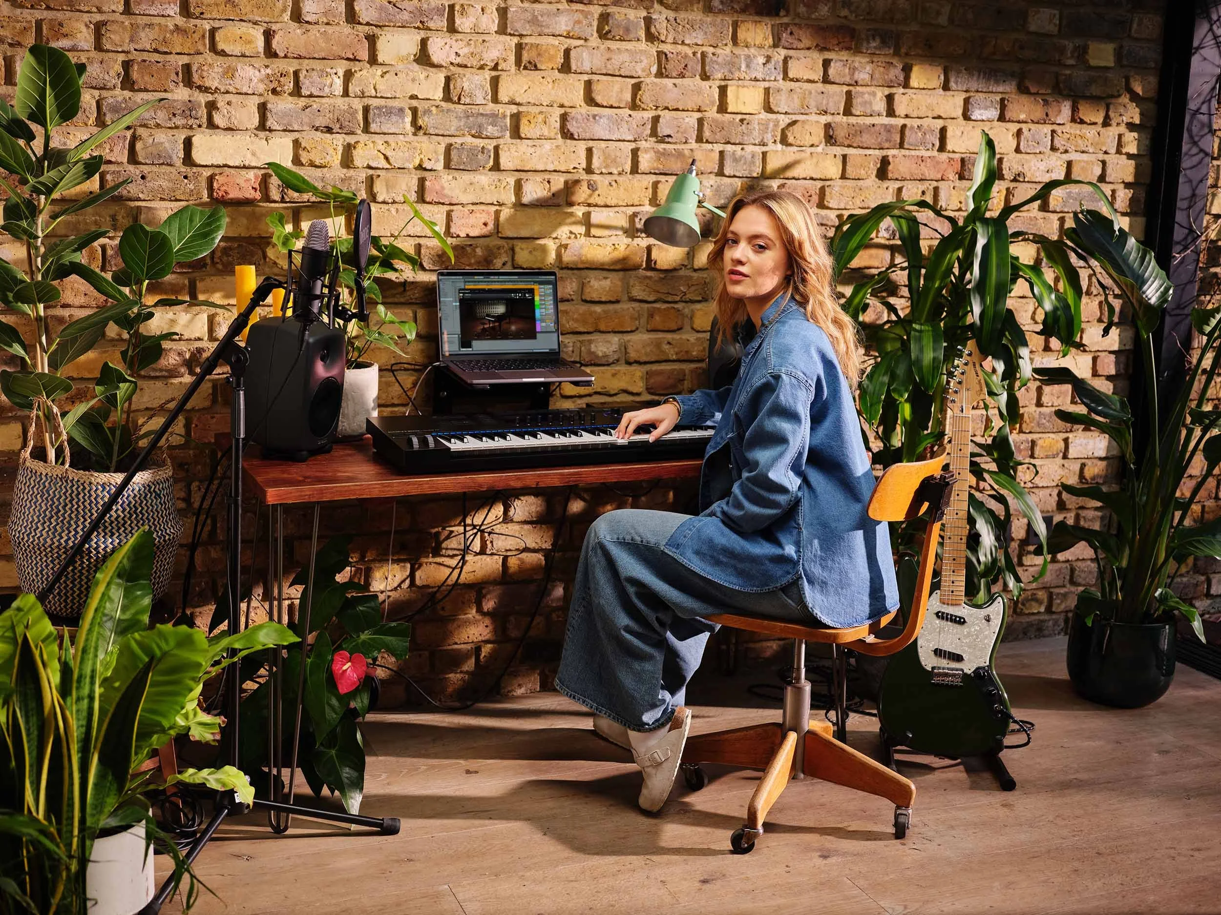 A young women sits at her home desk whilst using and playing Native Instruments software and hardware which are used for music production, sound design, performance and DJing