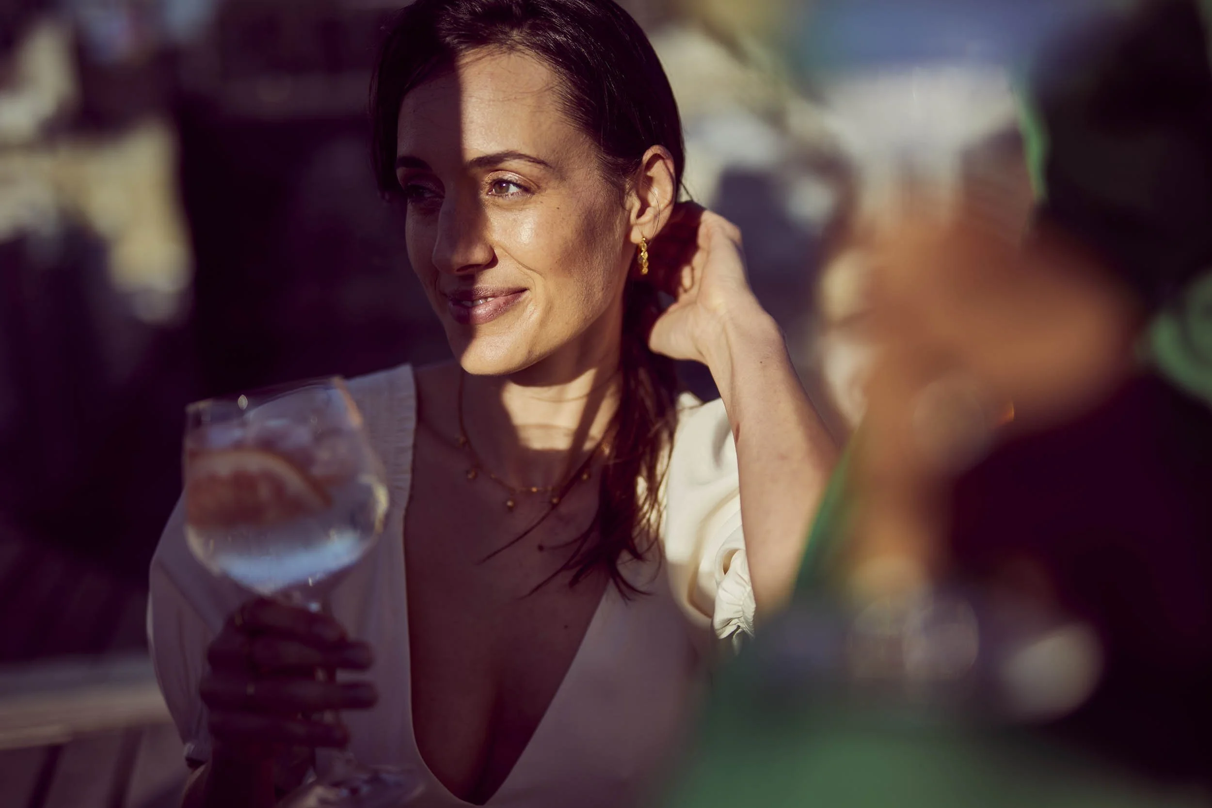 A young women holds a large glass of gin and tonic as the sun hits her face on a rooftop in this lifestyle image by Jon Enoch