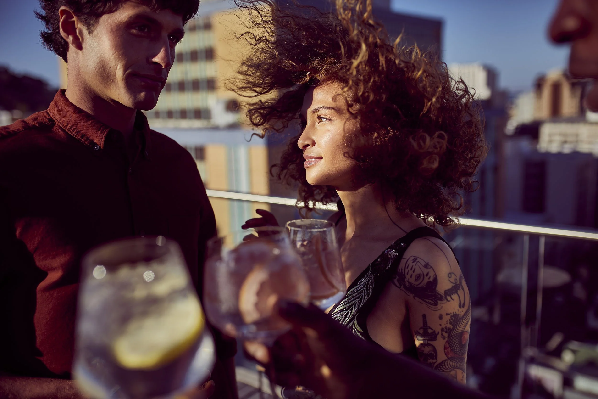 A young couple enjoy drinks on a rooftop in Cape Town as the sun sets over the city in this lifestyle images by photographer Jon Enoch