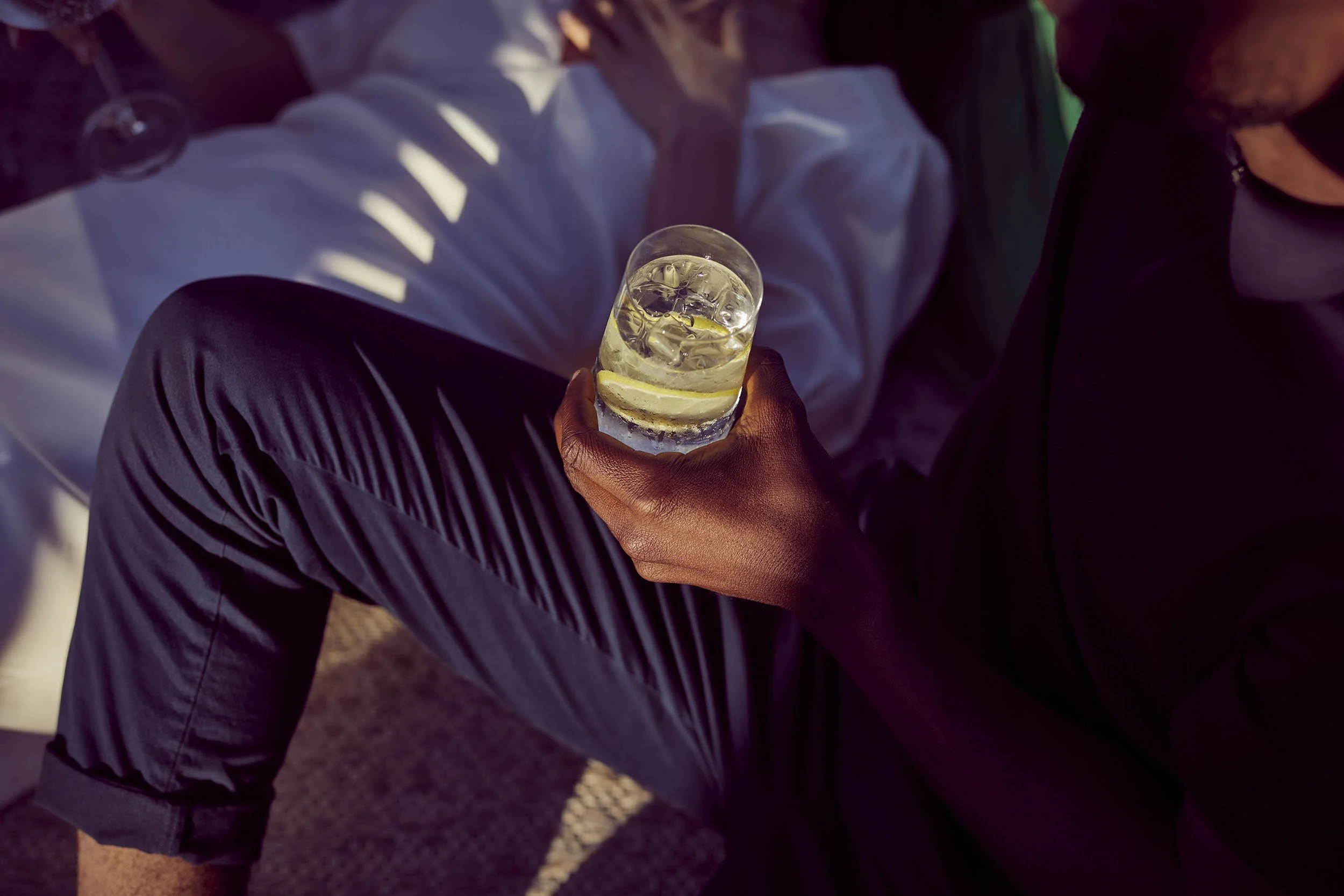 A mans hand holds a gin and tonic on the roof of a tall building in the late summer sun - lifestyle image by Jon Enoch
