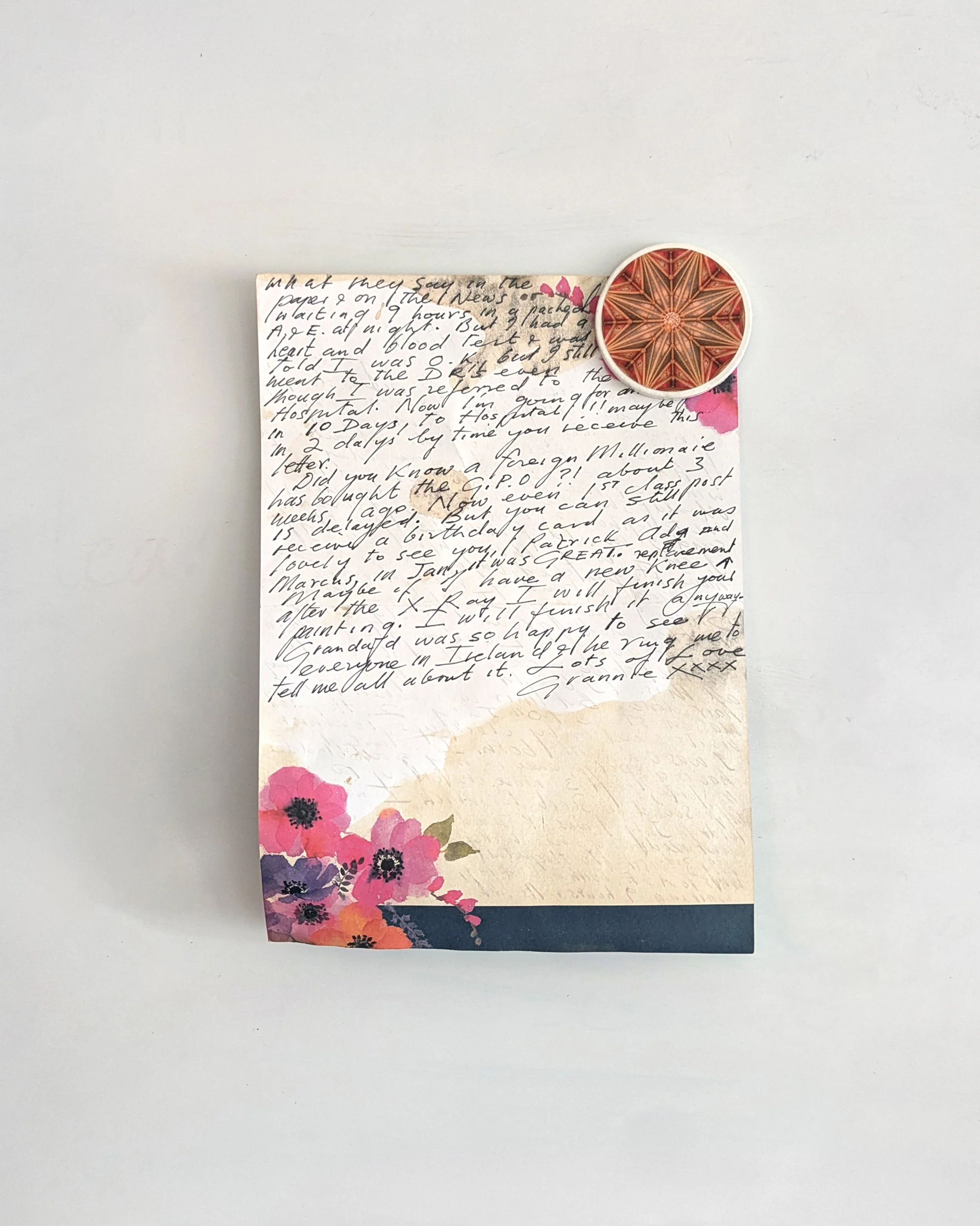 A handwritten letter on decorative paper with pink and purple flowers, a dark blue border, and a single copper-coloured clockwork design magnet from OH Arts holds the top corner. Bespoke artist stationery UK.