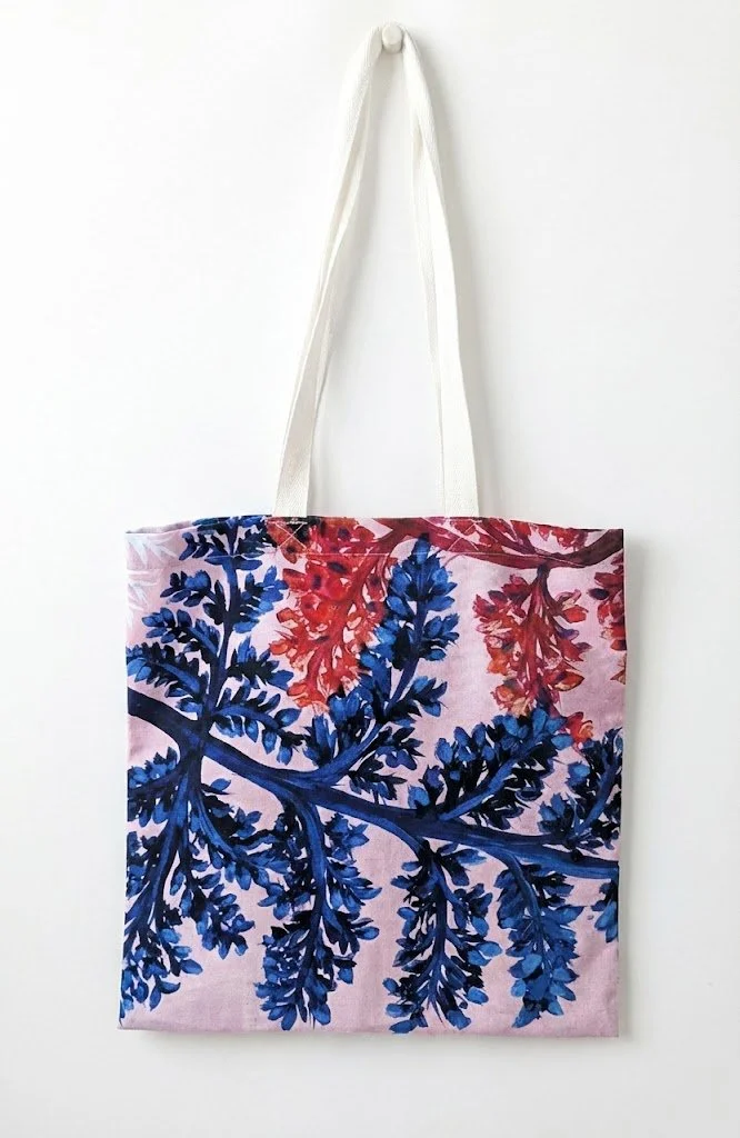 A full-length custom printed tote bag by OH Arts, featuring an intricate blue and red fern leaf pattern on a pink background, ideal for artist giftware UK.