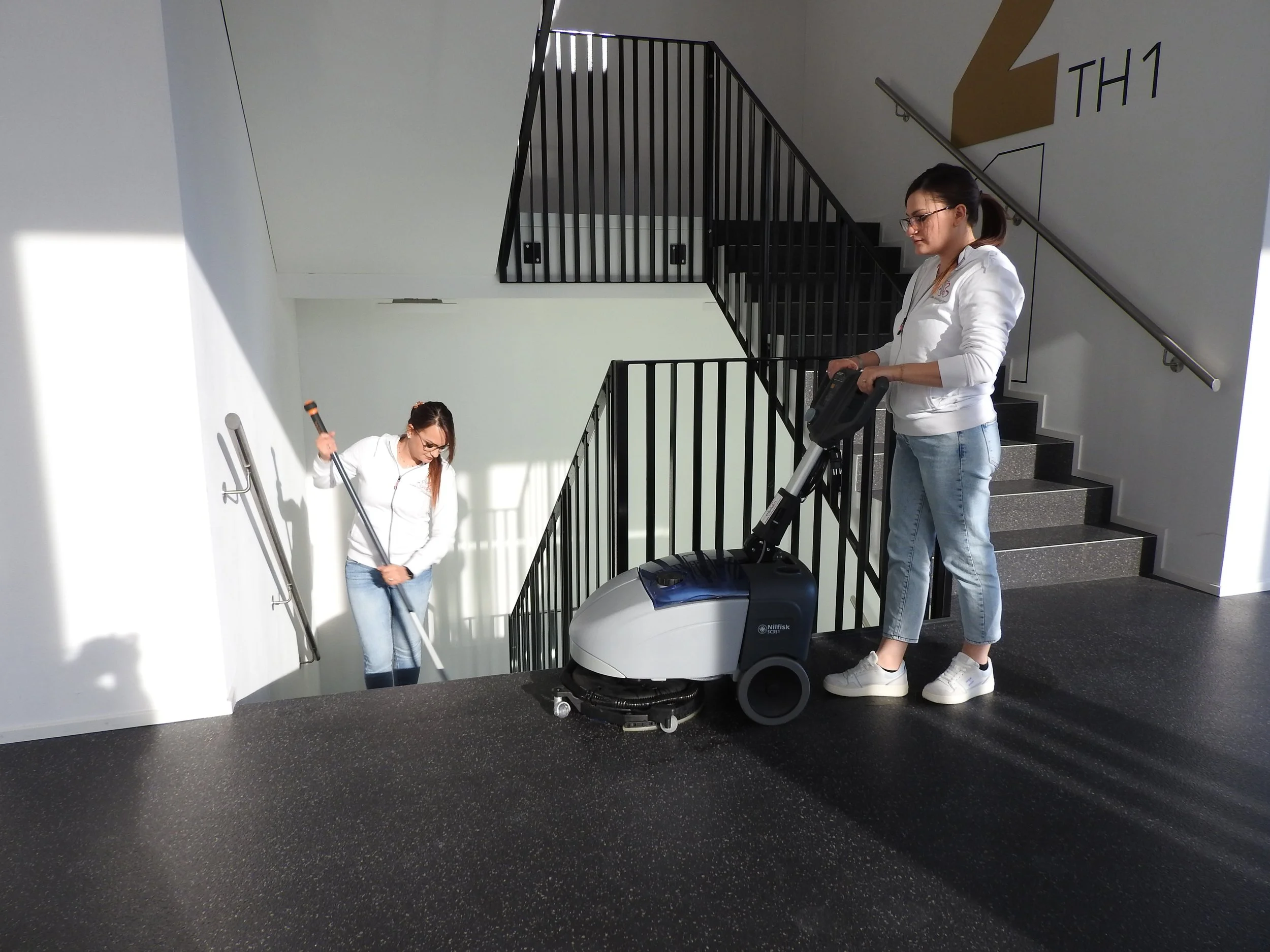 Zwei Frauen reinigen eine Treppe in einem Gebäude mit einer Spezial-Reinigungsmaschine.