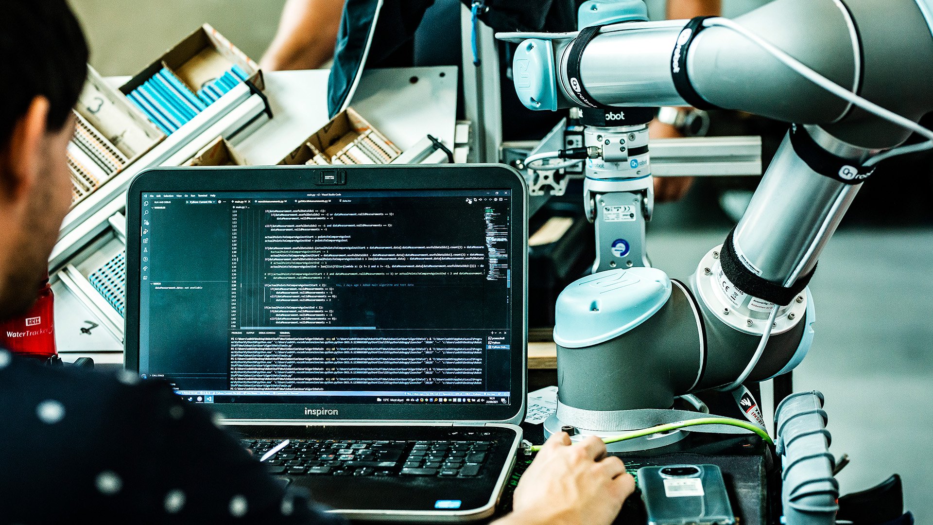Person working on a laptop with code next to a robot arm, illustrating AI transformation and AI adoption in business