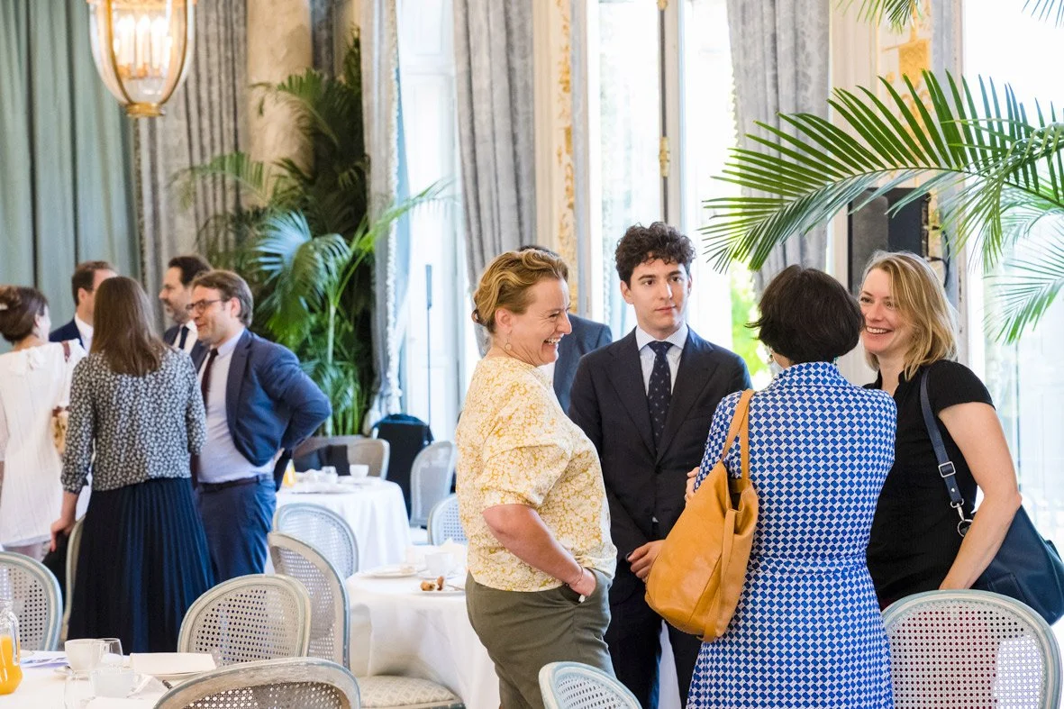 Groupe de personnes discutant et souriant dans une salle élégante avec des plantes vertes et de grandes fenêtres.