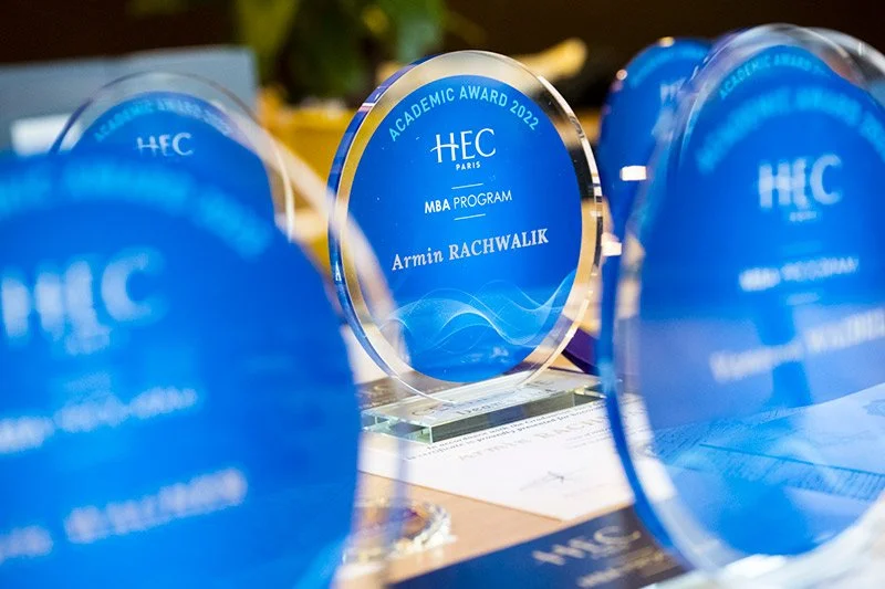 Trophées en verre bleus avec inscription pour le prix académique 2022 de l'HEC Paris, programme MBA, au centre de l'image.