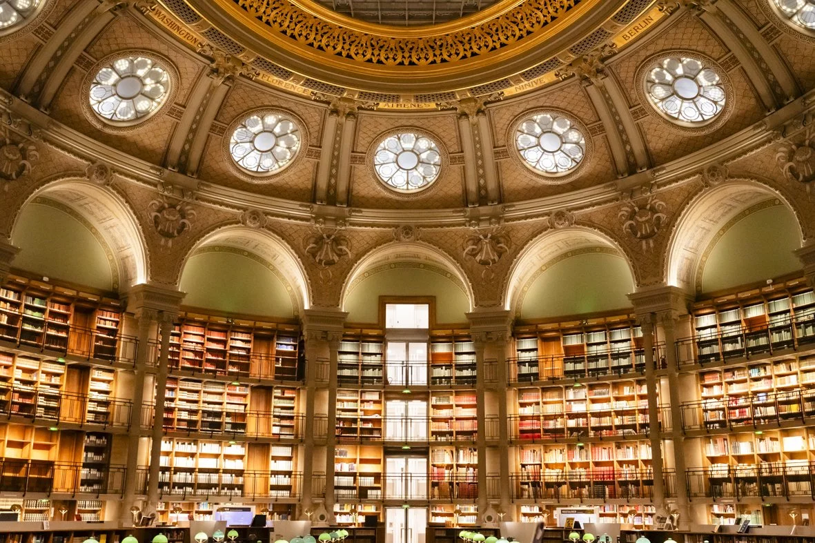 Une bibliothèque élégante avec une grande coupole lumineuse au plafond, des étagères en bois remplies de livres et des tables de lecture.