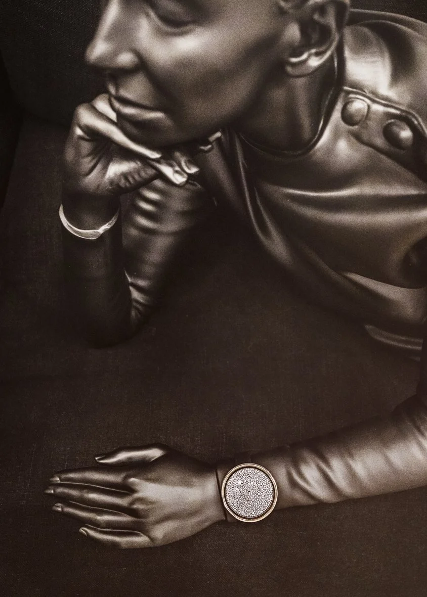 Portrait en noir et blanc d'une femme élégante portant des gants en cuir, une montre à bracelet métallique, et une veste en cuir, posant avec le visage légèrement penché et la main sous le menton.