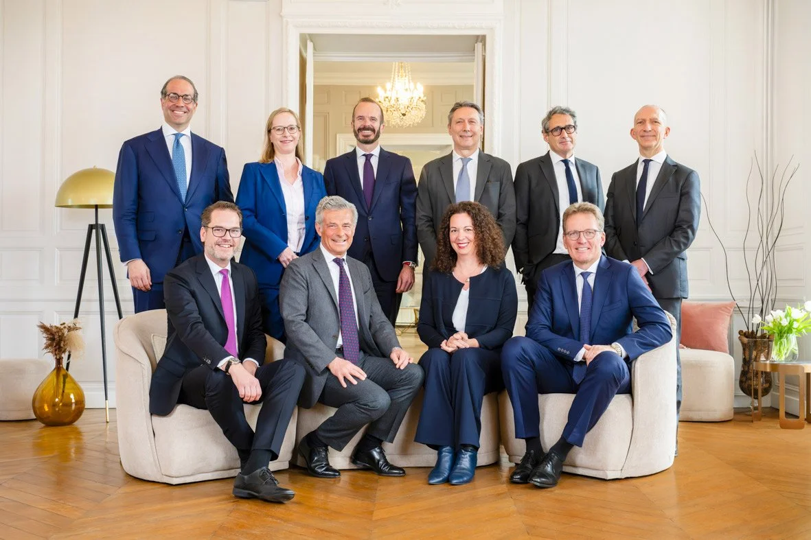 Groupe de dix personnes en costume dans un salon élégant, posant pour une photo de groupe.