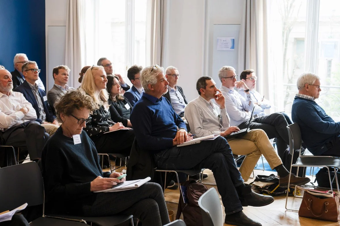 Groupe de personnes assises en salle lors d'une conférence, certaines prennent des notes ou utilisent leur téléphone.