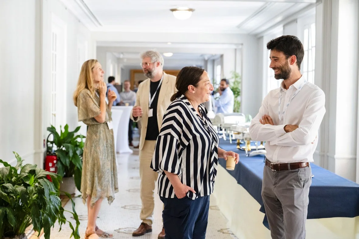 Groupe de personnes discutant et souriant lors d'une conférence ou d'un événement professionnel dans une salle bien éclairée.