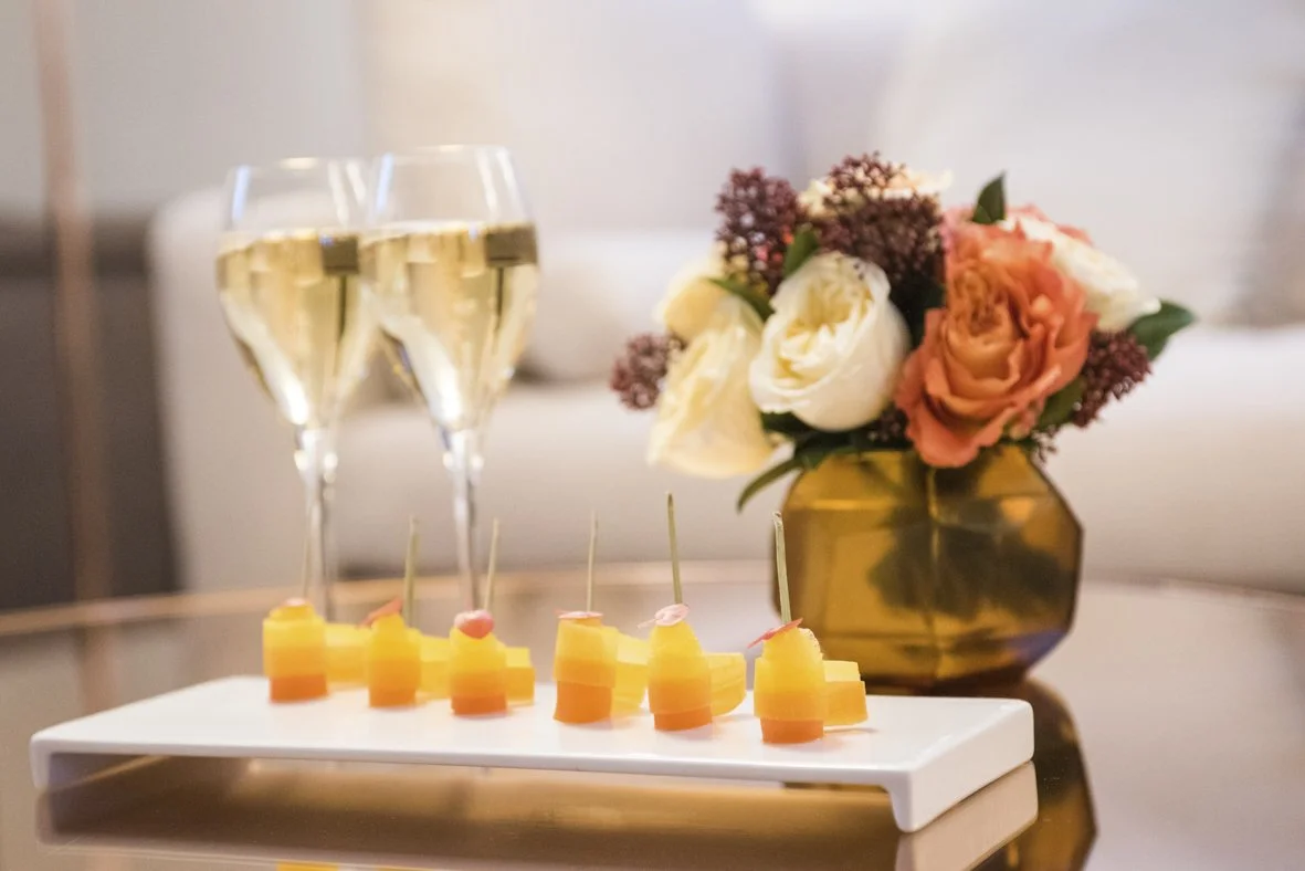 Deux flûtes de champagne, un plateau de bouchées de fromage, et un vase avec des fleurs colorées