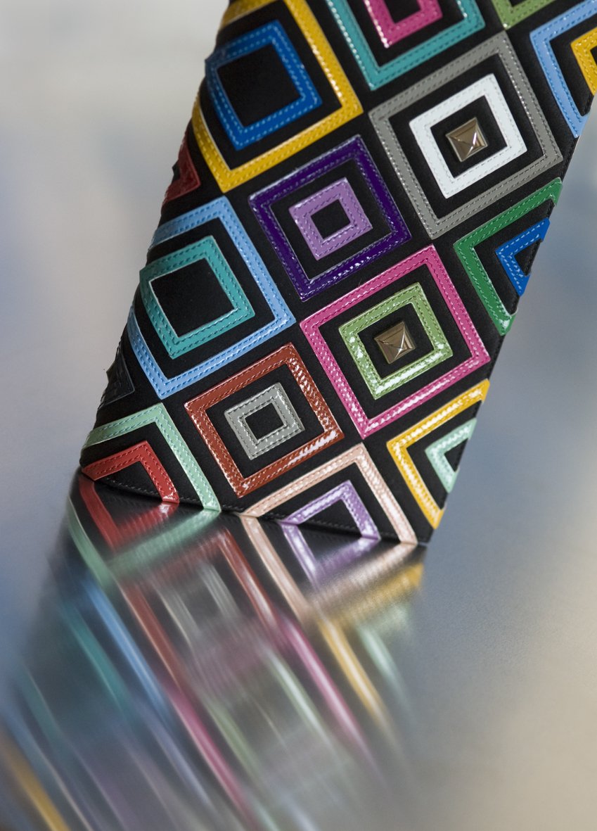 Une chaussure avec un motif coloré de carrés en relief, posée sur une surface réfléchissante.