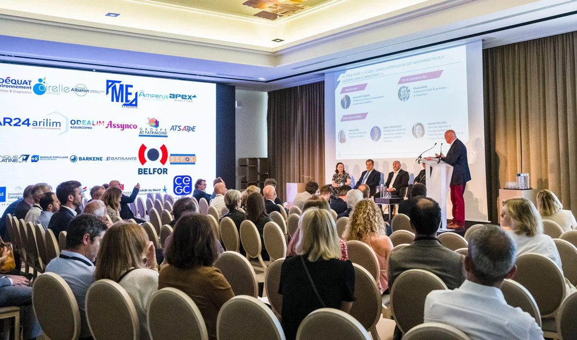 Conférence avec un public nombreux, un panel de quatre personnes sur scène, deux femmes et deux hommes, présentation projection sur grand écran et affichage de logos d'entreprises.