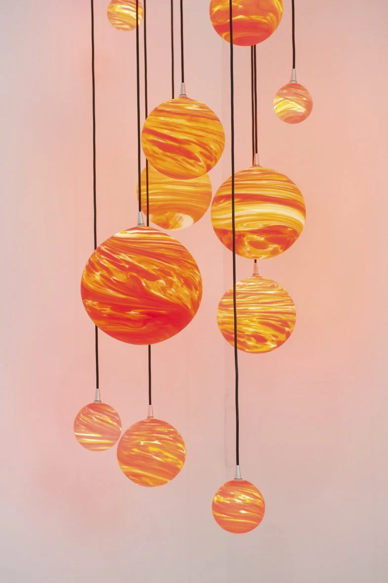 Suspension de lampes rondes orange et jaunes avec un fond rose clair.