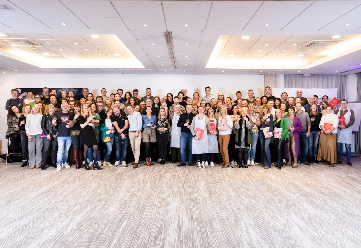 Groupe de personnes posant pour une photo dans une salle, certaines tenant des livres ou des cadeaux, ambiance convivial et festive.
