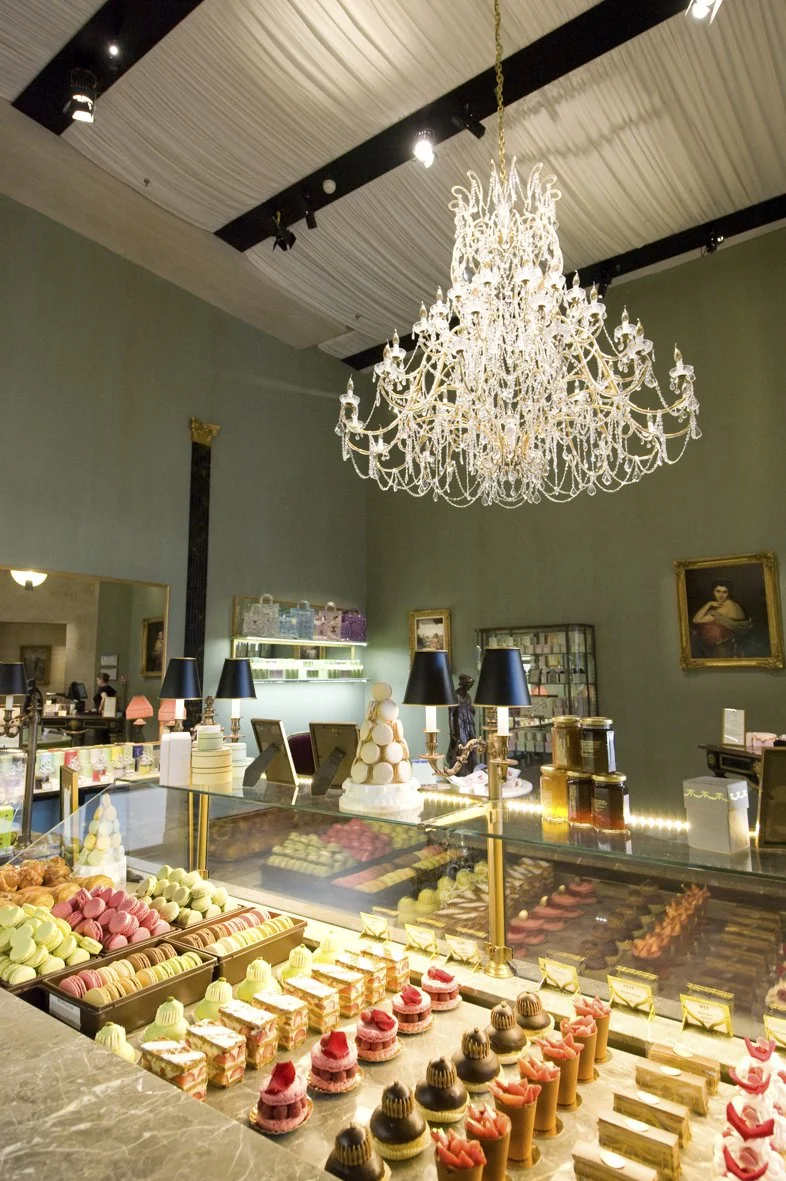 Vitrine de pâtisseries colorées dans une boulangerie élégante, avec un grand chandelier au plafond.