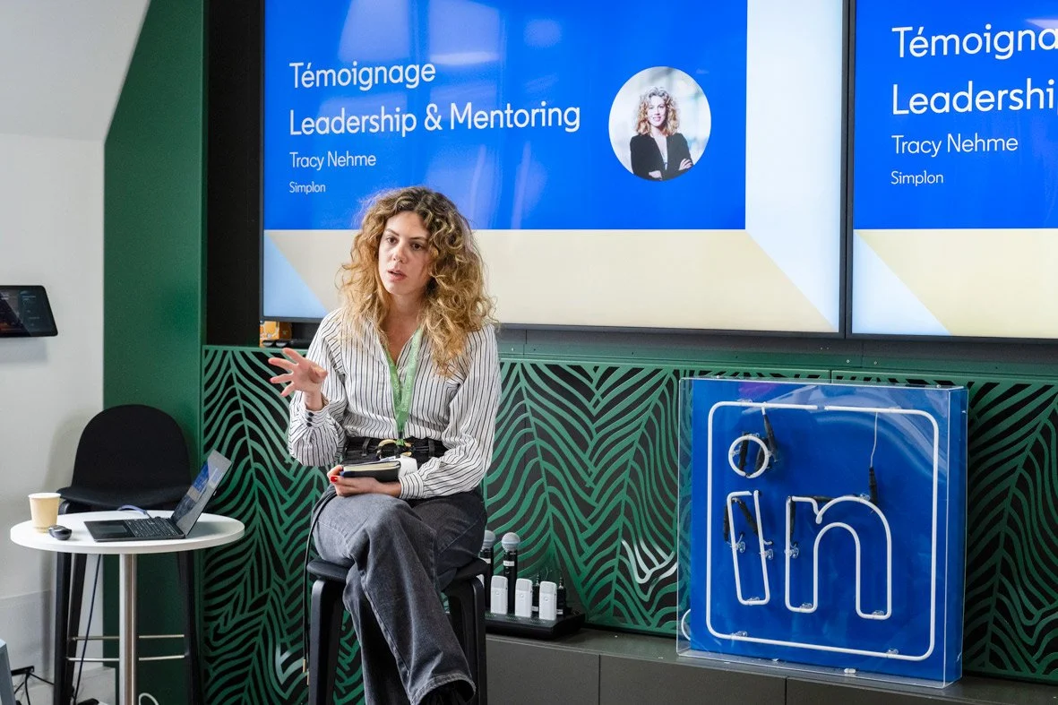 Femme donnant une présentation sur le leadership et le mentorat, avec un écran affichant son nom et le sujet, dans une salle de conférence équipée de matériel technologique et d'une signalisation LinkedIn.