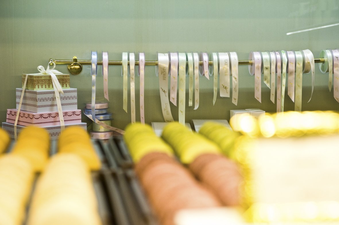 Présentation de rubans et rouleaux de papier dans une boutique de décoration ou de mode, avec des couleurs pastel et des boîtes décoratives.